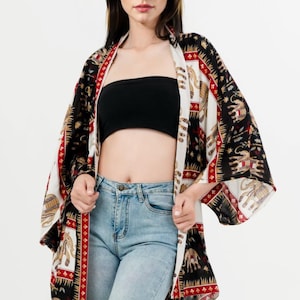Pu&ograve; includere: Kimono fantasia con un design nero, bianco e rosso con elefanti. L'indumento aperto &egrave; indossato sopra un top a tubo nero e jeans blu chiaro. Le maniche del kimono sono ampie e fluide.