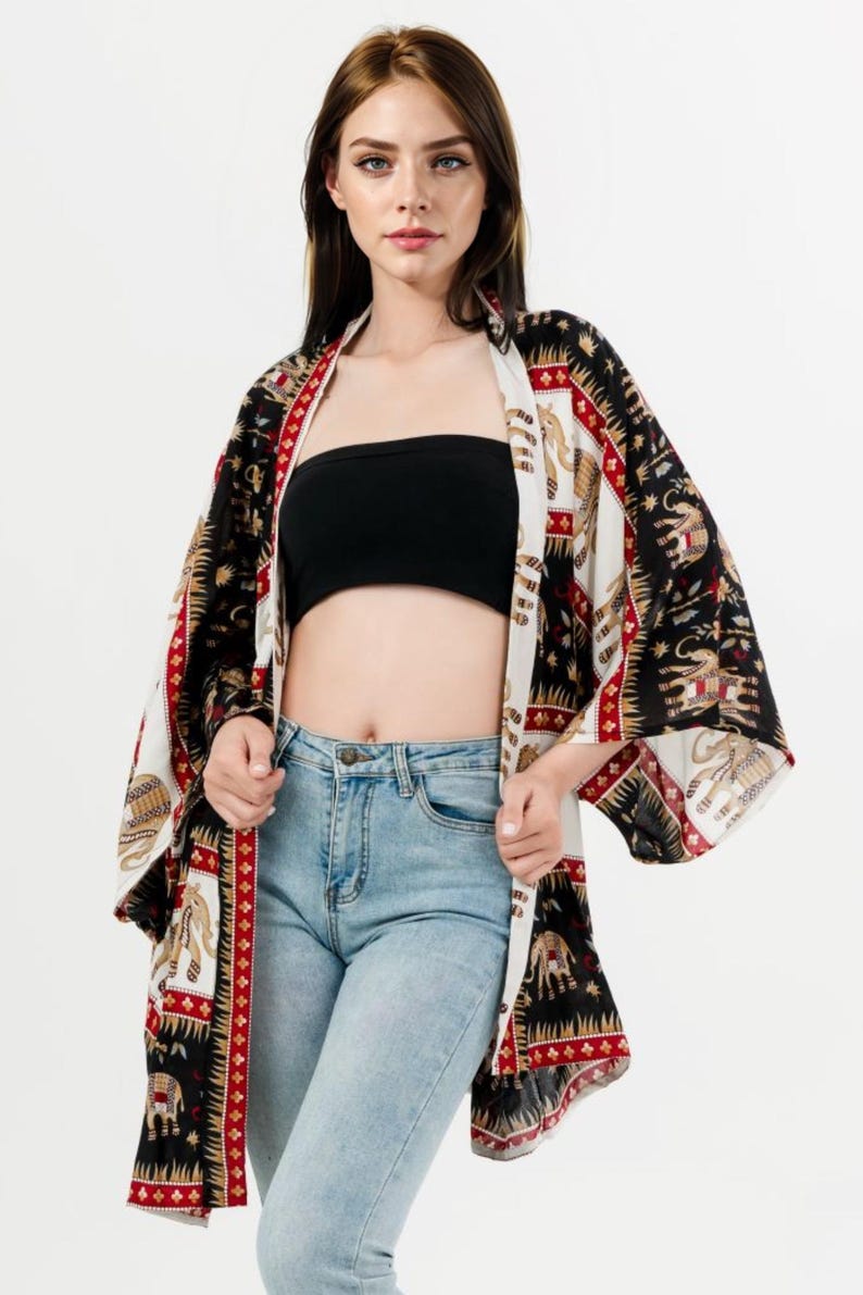 Pu&ograve; includere: Kimono fantasia con un design nero, bianco e rosso con elefanti. L'indumento aperto &egrave; indossato sopra un top a tubo nero e jeans blu chiaro. Le maniche del kimono sono ampie e fluide.
