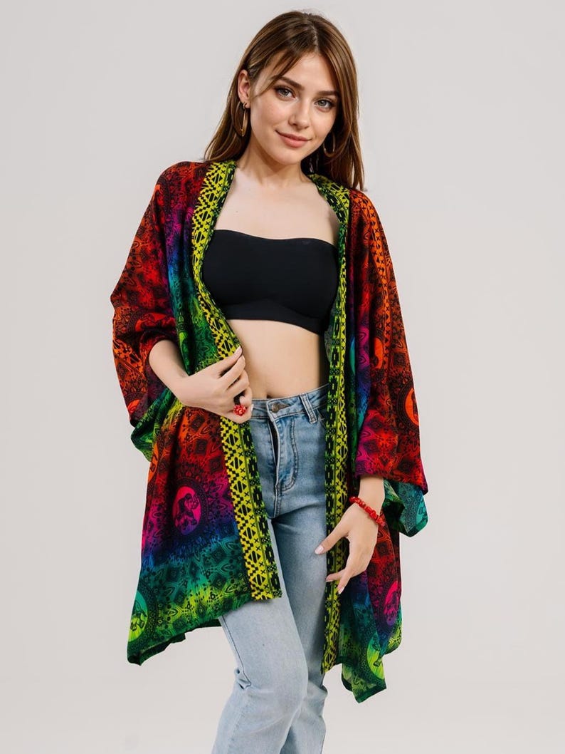 Pu&ograve; includere: Kimono aperto dai colori vivaci con un motivo arcobaleno. Il capo presenta un mix di tonalit&agrave; rosse, arancioni, gialle, verdi e blu, con un bordo decorativo. Indossato sopra un top nero e jeans azzurri.
