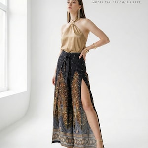 May include: A woman wearing a gold halter top and black palazzo pants with a peacock feather design. The pants have high slits on the sides. The model is 5.9 feet tall. The top is a solid gold color.