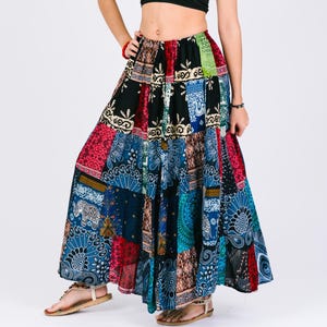 May include: A long, multi-coloured patchwork skirt with a black background. The skirt features a variety of patterns, including paisley, floral, and geometric designs. The skirt is made from a lightweight fabric and has a flowing silhouette.