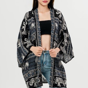 Pu&ograve; includere: Kimono a fantasia bianco e nero con motivi a elefante. Il kimono aperto presenta un design dettagliato con accenti blu. L'indumento &egrave; indossato sopra un top nero e jeans blu, creando un look a strati.