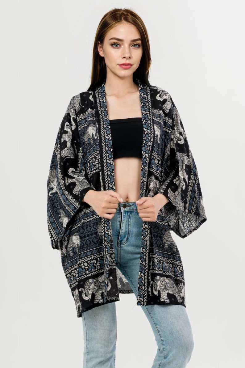 Pu&ograve; includere: Kimono a fantasia bianco e nero con motivi a elefante. Il kimono aperto presenta un design dettagliato con accenti blu. L'indumento &egrave; indossato sopra un top nero e jeans blu, creando un look a strati.