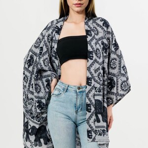 Pu&ograve; includere: Un kimono grigio con un motivo a elefanti neri. L'indumento a maniche lunghe e aperto sul davanti &egrave; indossato sopra un top nero e jeans azzurri. Il design del kimono presenta motivi ripetuti di elefanti e fiori.