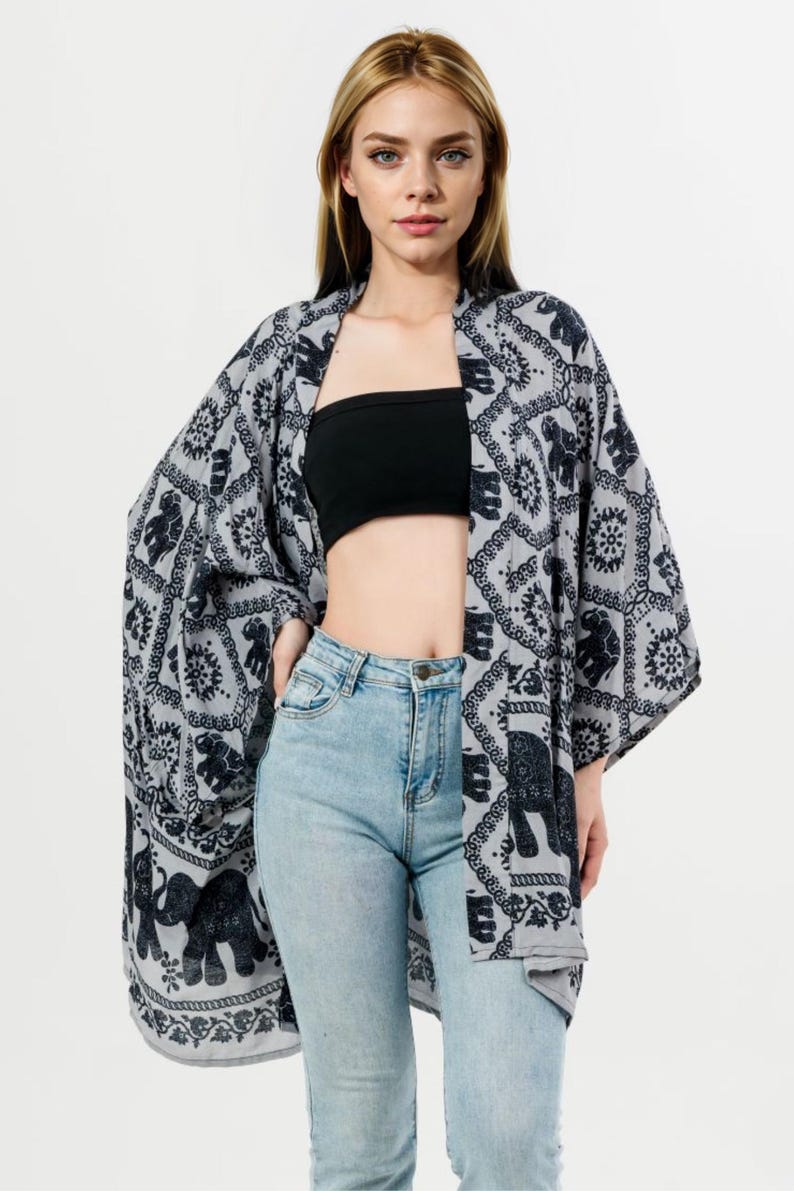 Pu&ograve; includere: Un kimono grigio con un motivo a elefanti neri. L'indumento a maniche lunghe e aperto sul davanti &egrave; indossato sopra un top nero e jeans azzurri. Il design del kimono presenta motivi ripetuti di elefanti e fiori.