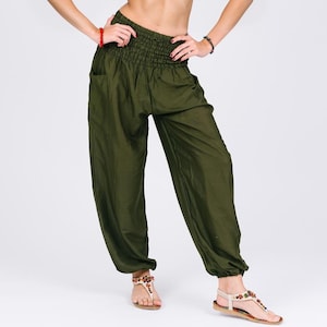 Può includere: Pantaloni harem verde oliva con vita arricciata e tasche. I pantaloni ampi hanno una silhouette rilassata e sono realizzati in un tessuto leggero. I pantaloni sono mostrati con sandali.