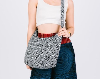 May include: A black and white geometric patterned tote bag with a long strap. The bag is worn over the shoulder of a person wearing a white crop top and a blue and red patterned skirt.