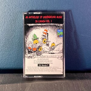 May include: A black cassette tape with a colourful cartoon illustration of musicians playing instruments. The tape is labelled "An Anthology of Underground Music in Canada Vol. 1 Featuring: 26 Bands!!" and lists the names of 26 bands.