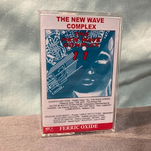 May include: A cassette tape for "The New Wave Complex 11" album. The cover has a blue and white design with a face and circuit board elements. The tape is in a clear plastic case.