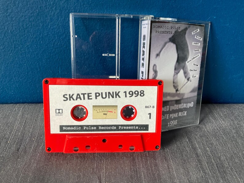K&ouml;nnte beinhalten: Ein rotes Kassettenband mit dem Titel "Skate Punk 1998" und dem Text "Nomadic Pulse Records Presents..." Das Kassettenband befindet sich in einem durchsichtigen Plastikgeh&auml;use mit einem kleineren Geh&auml;use, das eine Liste von Songs enth&auml;lt.