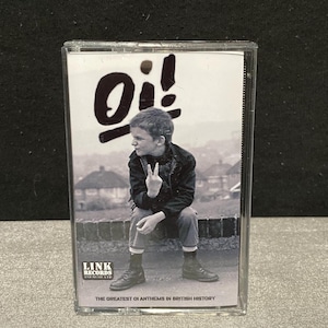 以下が含まれることがあります： 「Oi！」の文字が大きく書かれた白黒のカセットテープ。カバーにはピースサインをする人物が描かれています。「THE GREATEST OI ANTHEMS IN BRITISH HISTORY」の文字も確認できます。