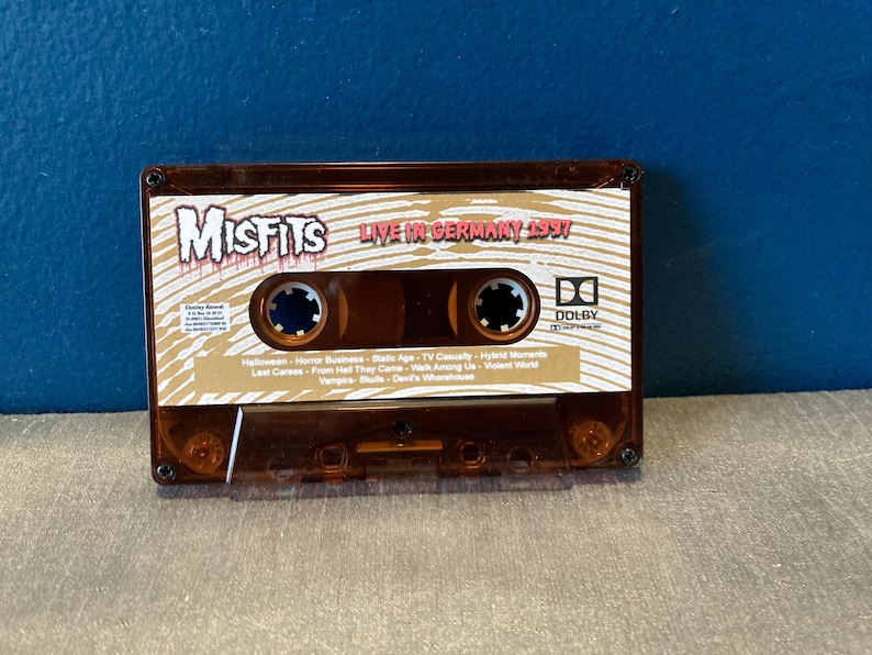 May include: A brown cassette tape with a gold label. The label has the text "Misfits Live in Germany 1997" and a list of songs. The cassette tape has a Dolby logo.