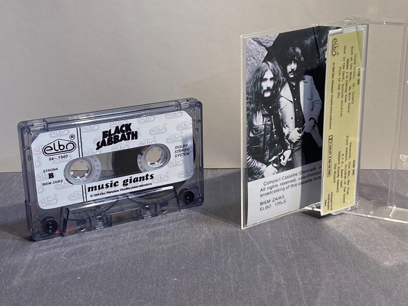 K&ouml;nnte beinhalten: Eine transparente Kassette des Albums "Music Giants" von Black Sabbath. Das Kassettengeh&auml;use ist transparent, mit dem Albumtitel und dem Bandnamen auf dem Etikett. Das Albumcover ist im Inneren sichtbar.