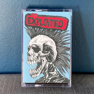 Pode incluir: Uma fita cassete com uma ilustração em preto e branco de uma caveira com um mohawk. O texto "The Exploited" está em letras vermelhas sobre um fundo azul.