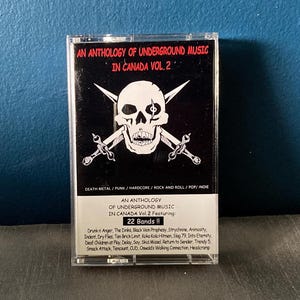 以下が含まれることがあります： 骸骨と交差した骨のモチーフが描かれた黒いカセットテープ。テープには「An Anthology of Underground Music in Canada Vol. 2 Featuring: 22 Bands!!」と表示され、22バンドの名前がリストされています。