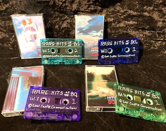 May include: Four cassette tapes and their corresponding plastic cases labeled Rare Hits of the 80s. The tapes are translucent teal, blue, purple, and green. Each tape features white text including volume numbers and 2001 Castle Communications.