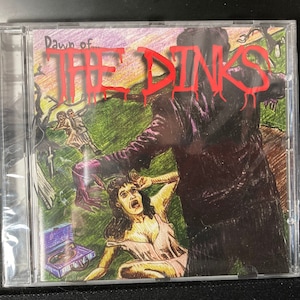 May include: A CD case featuring a colourful illustration of a person in a purple suit holding a woman in a pink dress. The text "Dawn of The Dinks" is written in red letters on the front of the case.