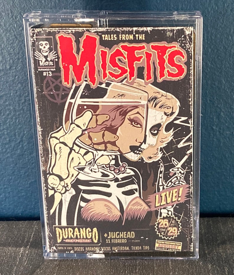 May include: A vintage-style concert poster for the Misfits, featuring a skull and a woman with a glass of liquid. The poster is in a clear plastic case. The text on the poster reads "Tales from the Misfits", "Durango", "Jughead", "11 Febrero", "Live!" and "26/29".