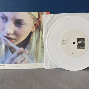 May include: White 7-inch vinyl record with a black and white label. The label has the text "track star 007" and "The Clocks 2/5 Series" on it. The record is in a white paper sleeve.