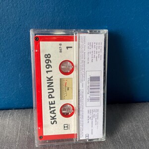 K&ouml;nnte beinhalten: Ein rotes Kassettenband mit dem Text "Skate Punk 1998" und einem Lautst&auml;rkemessger&auml;t. Das Band befindet sich in einem durchsichtigen Plastikgeh&auml;use.