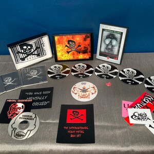 Może przedstawiać: Czarny zestaw pudełkowy z motywem czaszki i skrzyżowanych kości. Zestaw zawiera DVD, płyty CD i naklejki. Tekst na zestawie pudełkowym brzmi "The International Heavy Metal Box Set".
