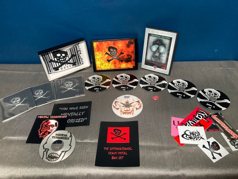 Może przedstawiać: Czarny zestaw pudełkowy z motywem czaszki i skrzyżowanych kości. Zestaw zawiera DVD, płyty CD i naklejki. Tekst na zestawie pudełkowym brzmi "The International Heavy Metal Box Set".