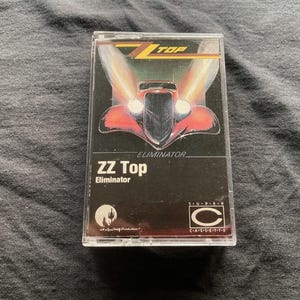 Puede incluir: Una taza de cerámica blanca con un asa negra y el texto "But First, Coffee" en negrita negra. La taza está sobre una superficie de madera. La taza parece tener una capacidad de unos 355 ml.