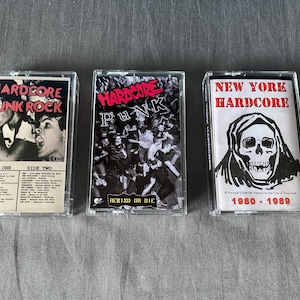 Op de afbeelding: Drie vintage cassettes. De hoezen tonen "HARDCORE PUNK ROCK", "HARDCORE PUNK" en "NEW YORK HARDCORE" in rode en zwarte tekst. De cassettes hebben zwart-wit beelden. De cassettehoesjes zijn van transparant plastic.