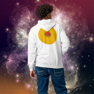 Puede incluir: Sudadera con capucha blanca con un diseño circular amarillo en la espalda. El círculo tiene un patrón floral rojo y naranja en su interior. La sudadera tiene el texto "I am a little more" impreso en la manga derecha.