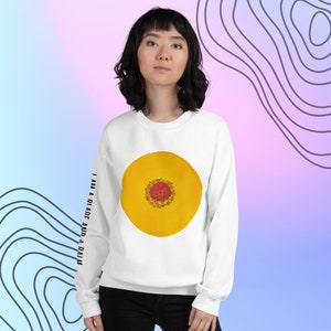 May include: White sweatshirt with a yellow circle with a red center and the text "I am a blade and a palm" on the sleeve.