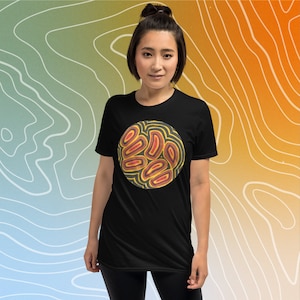 Puede incluir: Una camiseta negra con un diseño circular que presenta formas abstractas en tonos rojos, naranjas y amarillos. El diseño está sobre un fondo oscuro.