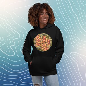 Puede incluir: Sudadera con capucha negra con un diseño gráfico circular que presenta un patrón abstracto amarillo y naranja. El gráfico está centrado en la parte delantera de la sudadera.