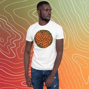 Puede incluir: Una camiseta blanca con un diseño circular que presenta un fondo negro y formas abstractas amarillas y rojas.