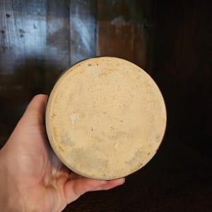 Puede incluir: Base de jarra redonda de cer&aacute;mica hecha a mano, de color marr&oacute;n claro. La jarra tiene un borde marr&oacute;n oscuro y una superficie ligeramente texturizada. La jarra est&aacute; sujeta en la mano de una persona.