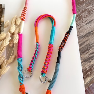 Könnte beinhalten: Eine Sammlung farbenfroher, geflochtener Schlüsselbänder in verschiedenen Pink-, Orange-, Blau- und Schwarztönen. Jedes Schlüsselband hat einen silbernen Ring und einen herzförmigen Anhänger. Die Schlüsselbänder werden auf einer weißen Oberfläche präsentiert.