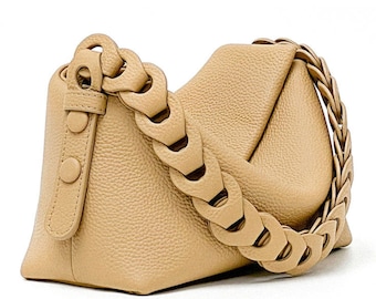 Può includere: Una borsa a tracolla in pelle color beige con una tracolla a catena spessa. La borsa ha una forma morbida e rilassata e una chiusura a lembo.