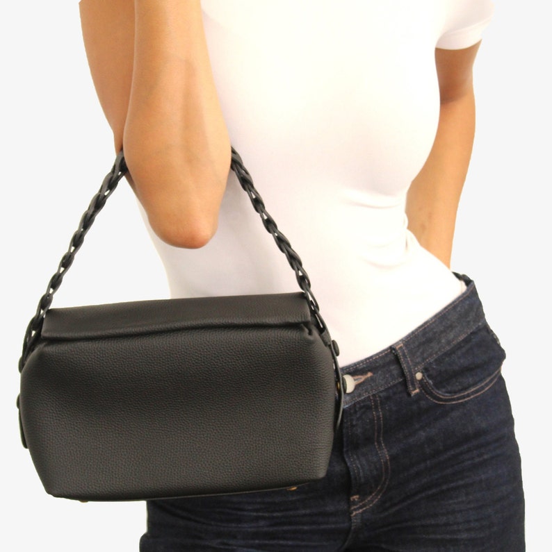 May include: A black leather handbag with a braided strap. The bag has a flap closure and a structured shape.