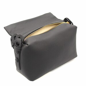 May include: Black leather zippered pouch with a gold zipper and a decorative black leather strap with a knotted design.