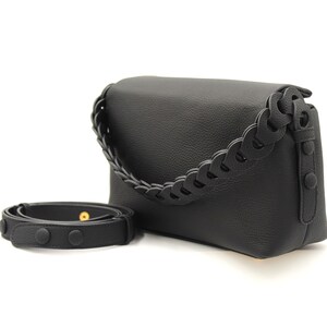 May include: Black leather shoulder bag with a braided strap. The bag has a flap closure and a small pocket on the front.