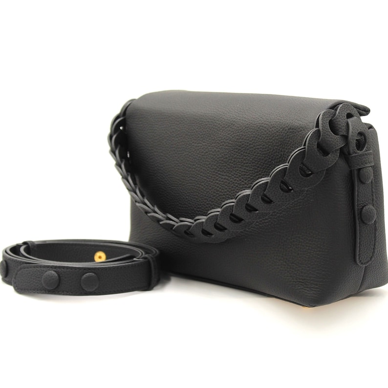 May include: Black leather shoulder bag with a braided strap. The bag has a flap closure and a small pocket on the front.
