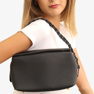 May include: A black leather handbag with a braided strap. The bag has a rectangular shape and a textured finish.