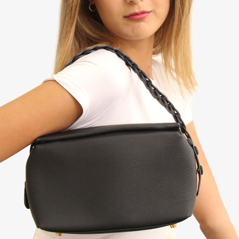 May include: A black leather handbag with a braided strap. The bag has a rectangular shape and a textured finish.