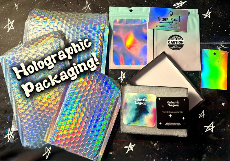 Pode incluir: Uma cole&ccedil;&atilde;o de envelopes almofadados hologr&aacute;ficos, uma bolsa verde-menta, um cart&atilde;o de agradecimento e uma caixa de joias preta contendo dois cart&otilde;es quadrados com o texto Galactic Lagoon. O texto Holographic Packaging est&aacute; em branco.