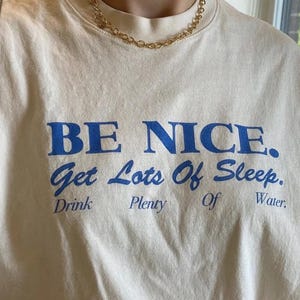 May include: A white t-shirt with blue text that reads "BE NICE. Get Lots Of Sleep. Drink Plenty Of Water."