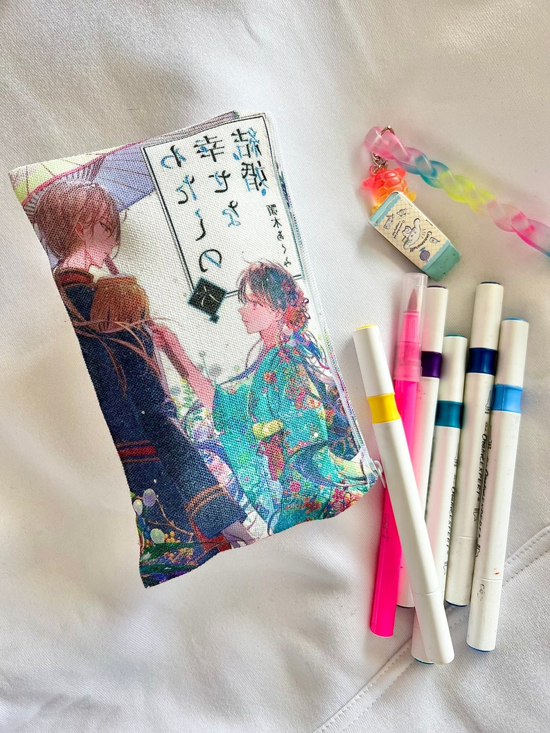 May include: A white canvas pouch with a colorful anime illustration and Japanese text. The text reads "桜降る夜に幸せを" which translates to "Happiness in the night of cherry blossoms falling". The pouch is lying on a white surface with several colorful markers.