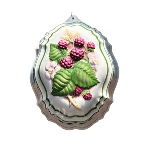 Puede incluir: Un molde de cerámica blanco con borde festoneado, con un diseño en relieve de frambuesas, hojas verdes y flores blancas. El molde tiene un borde a rayas verdes y blancas y un pequeño lazo de metal para colgar.