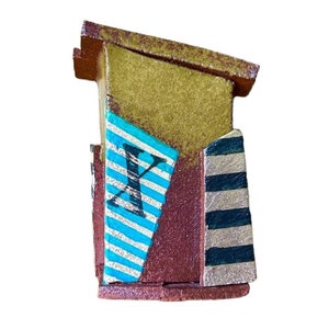 May include: A small wooden box with a gold, brown, and blue painted design. The box has a striped pattern on the side and the letter "X" on the front.