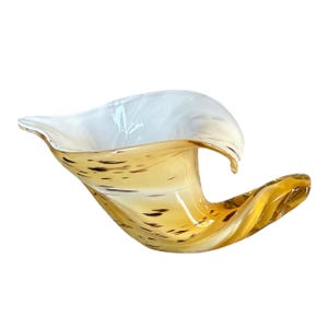 May include: A hand-blown glass vase with a unique wave-like design. The vase is made of clear glass with brown and white swirls and speckles. It is a beautiful and unique piece of art that would add a touch of elegance to any home.