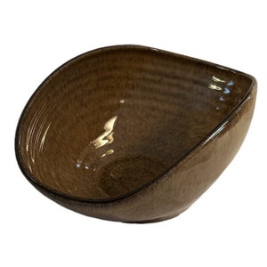 Könnte beinhalten: Eine braune Keramikschüssel mit leicht quadratischer Form und glänzender Oberfläche. Die Schüssel hat ein dezentes, strukturiertes Muster.