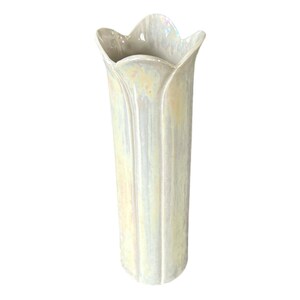 May include: A white ceramic vase with a scalloped rim and a pearlescent glaze. The vase has a tall, slender shape and is perfect for displaying flowers.